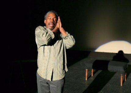 Actor LeLand Gantt closes his eyes, presses his palms together and leans his face against his hands onstage.