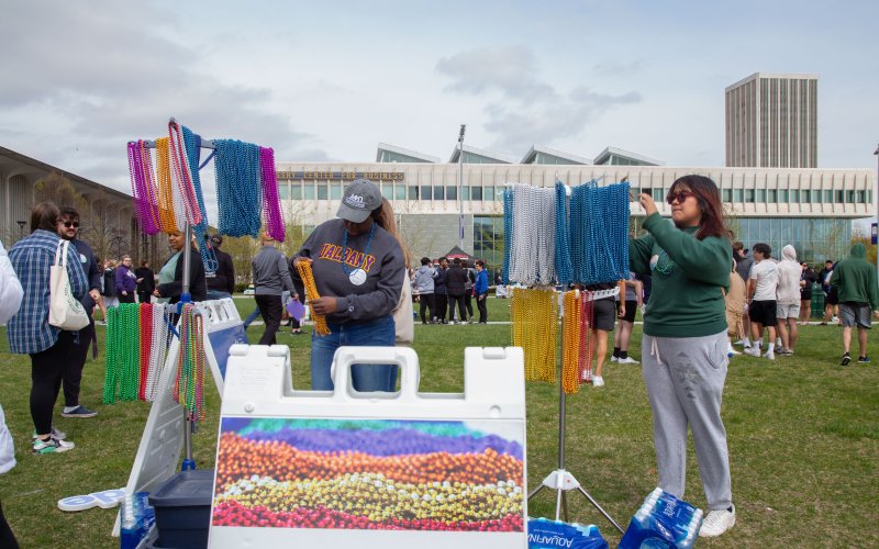 Students stand next two to racks of colorful beaded necklaces at the 2023 walk. The colors of the beads signify different connections someone might have to the issue of suicide. 