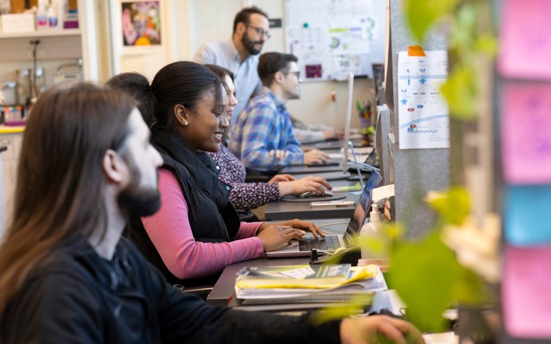 Student researchers sit in a row, working at a bank of computers. 