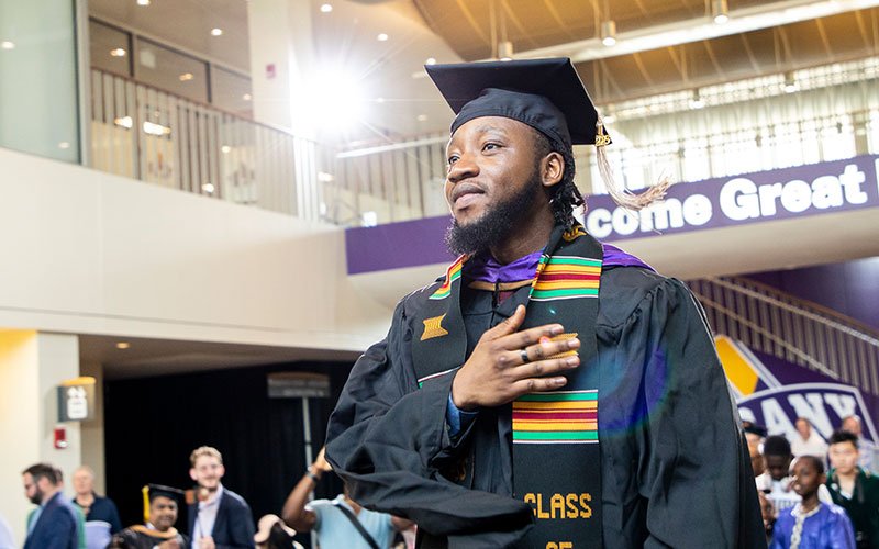 A masters graduate prepares to walk across a commencement stage in UAlbany's student center.