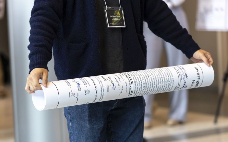 A person wearing a dark blue sweater and jeans rolls up a research poster at the end of the event.
