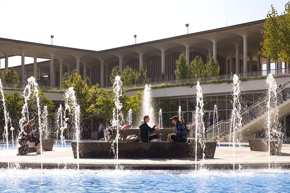 Students sit at the Main Campus fountain on a fall day.