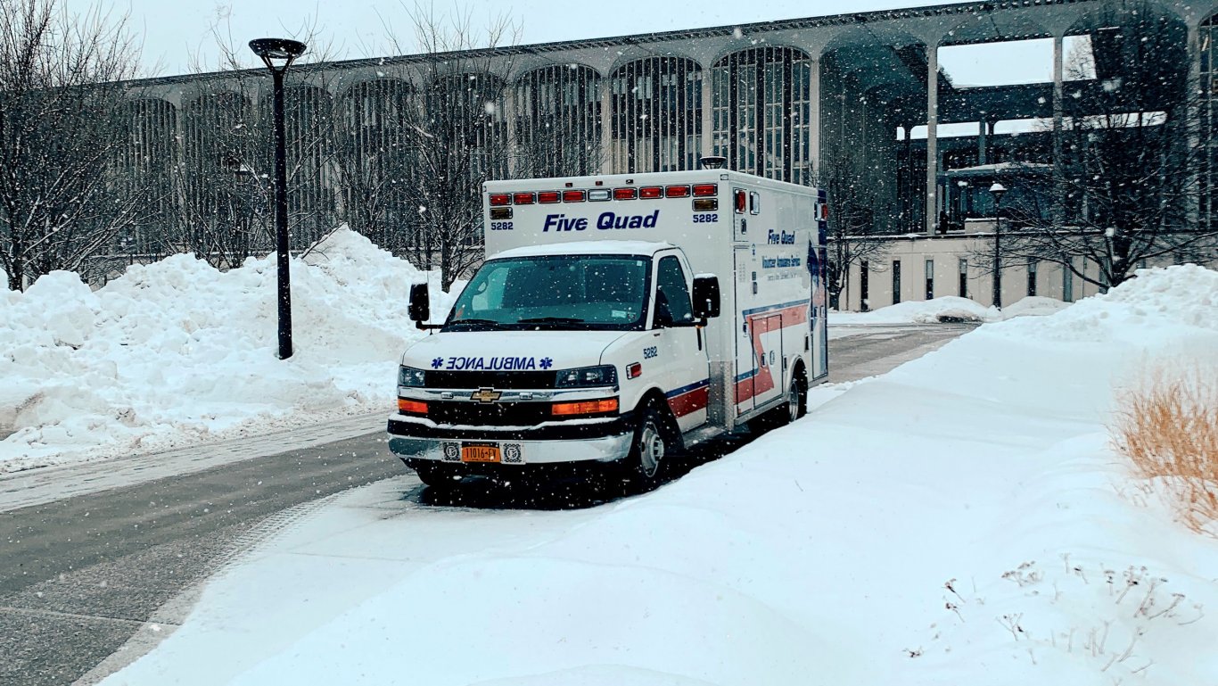 A Five Quad ambulance parked in front of an academic building in the falling snow