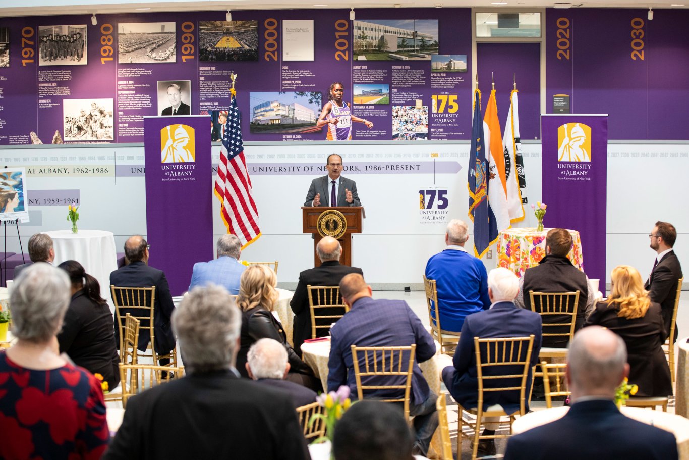 UAlbany President Havidán Rodríguez speaks at a podium in front of a room of people inside the University Hall atrium at UAlbany Showcase.