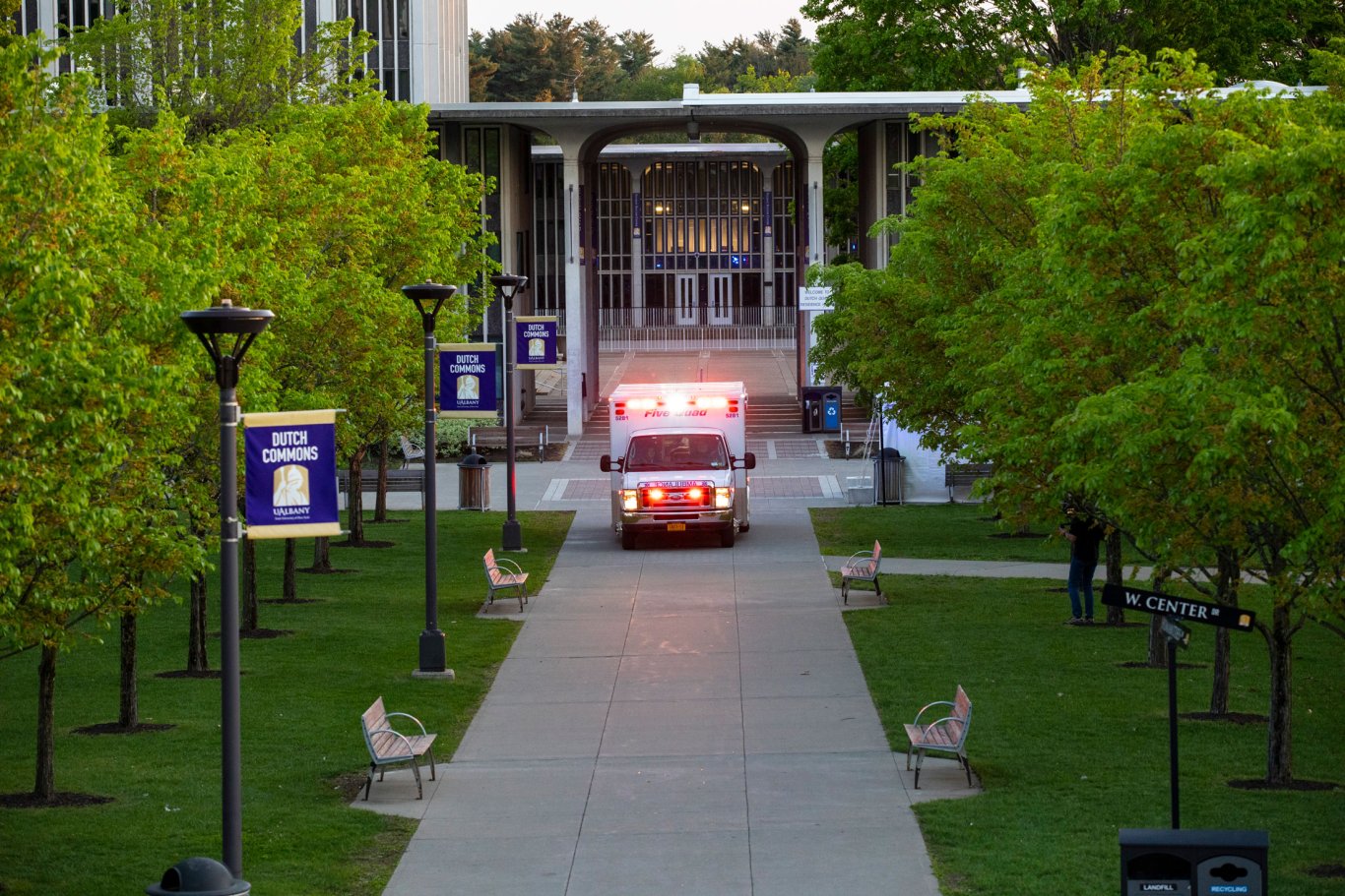 A Five Quad ambulance with emergency lights drives down the pathway lined with green grass and trees on Dutch Commons on the Uptown Campus.