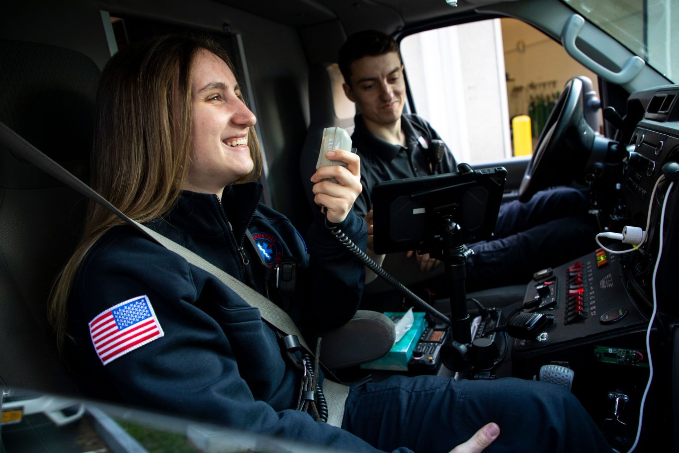 Two Five Quad crew members sit inside the front seat of the ambulance speaking on the handheld radio.
