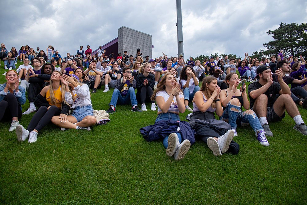 Students sitting in the grass watching the homecoming football game.