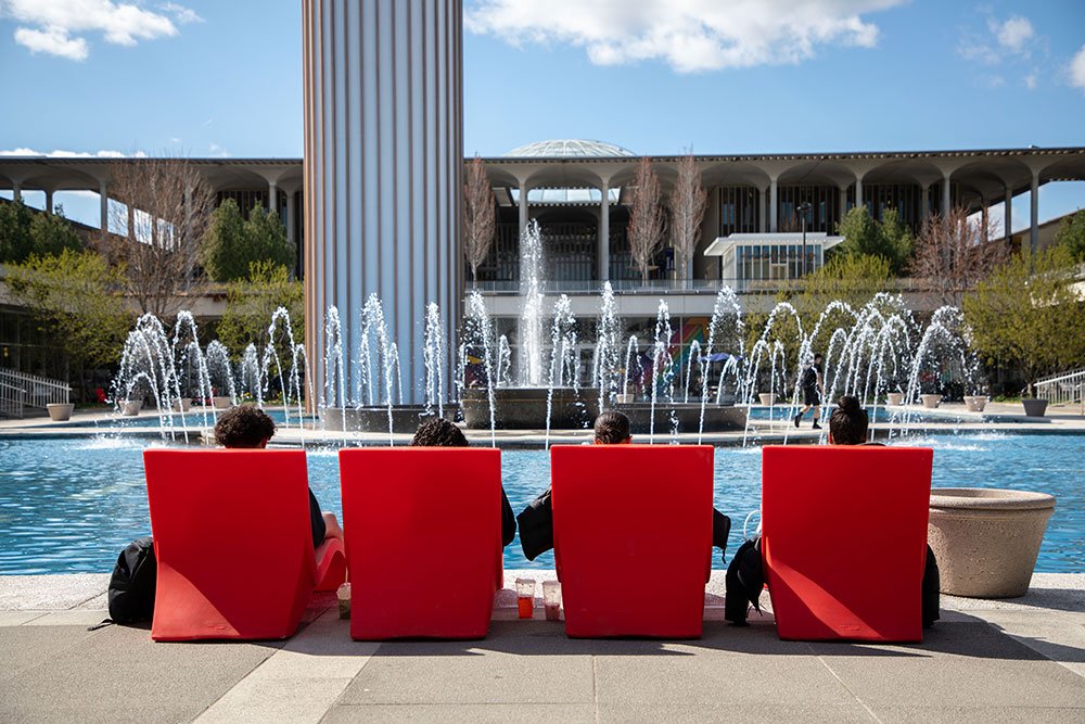 Students sitting outside in chairs by the fountain.