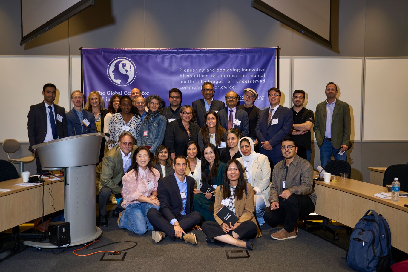 About 30 people pose for a photo in front of a GCAIMH Annual Summit banner.