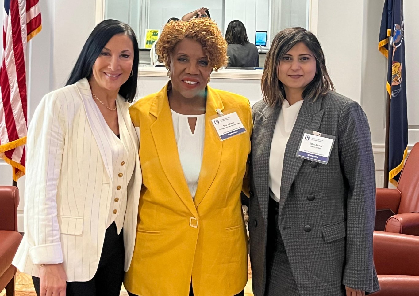 Three women wearing blazers and conference name tags pose for a photo together.