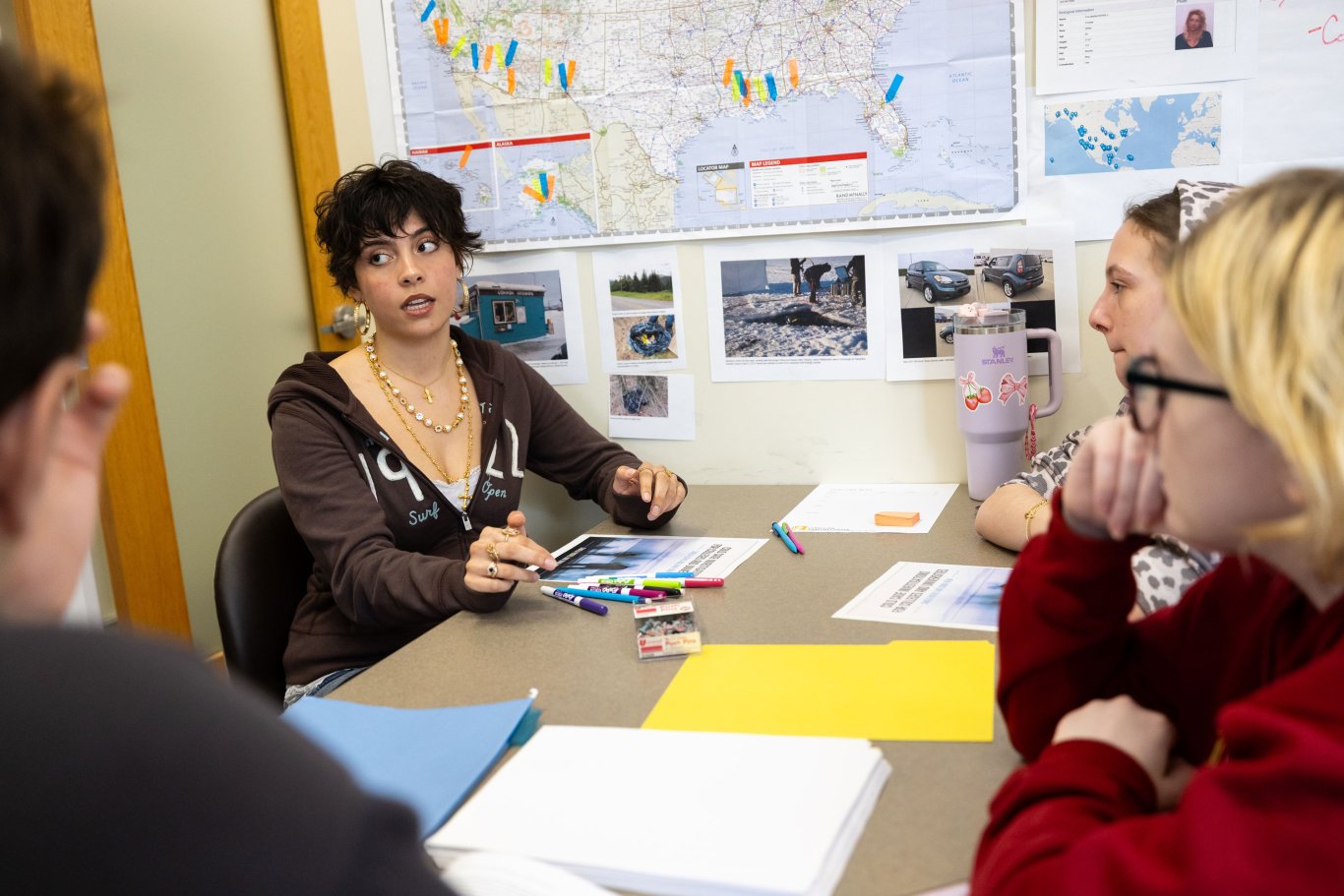 An image of three students sitting at a table with pieces of paper discussing matters.