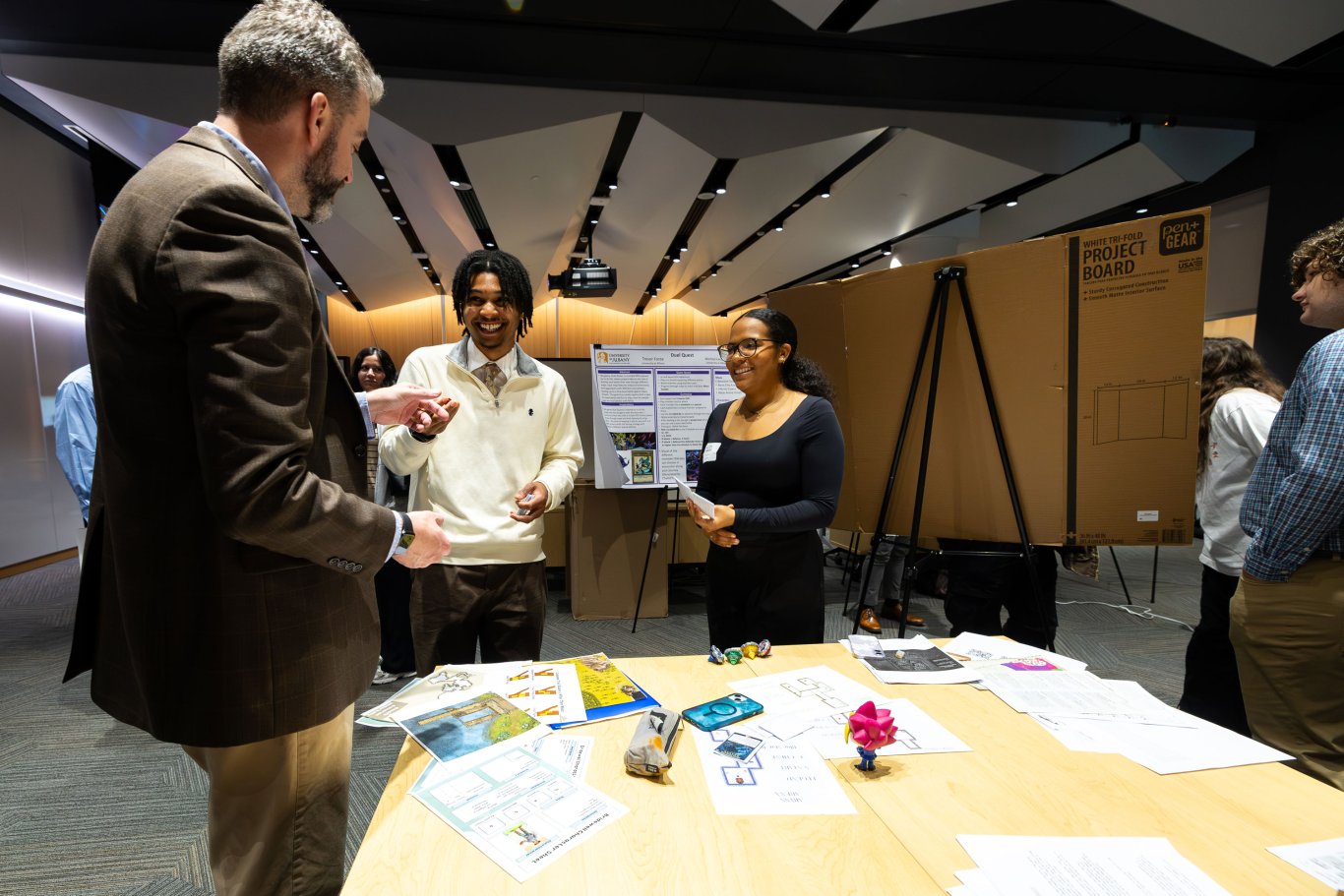 Two student presenters smile as they speak with a Showcase attendee about game design.