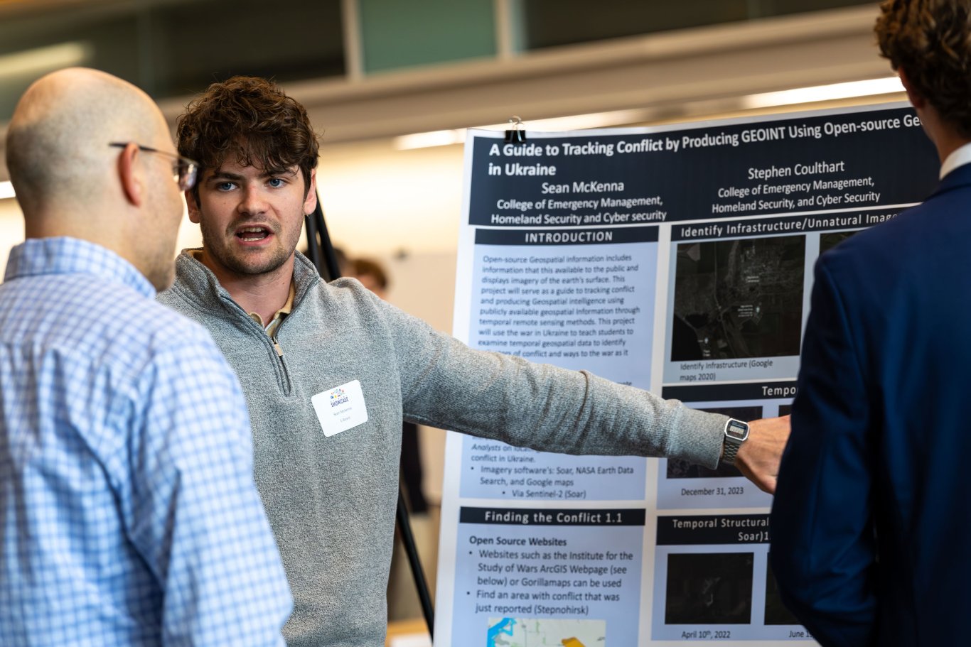 A student presenter gestures toward his research poster while speaking with a Showcase attendee about tracking conflict in Ukraine.