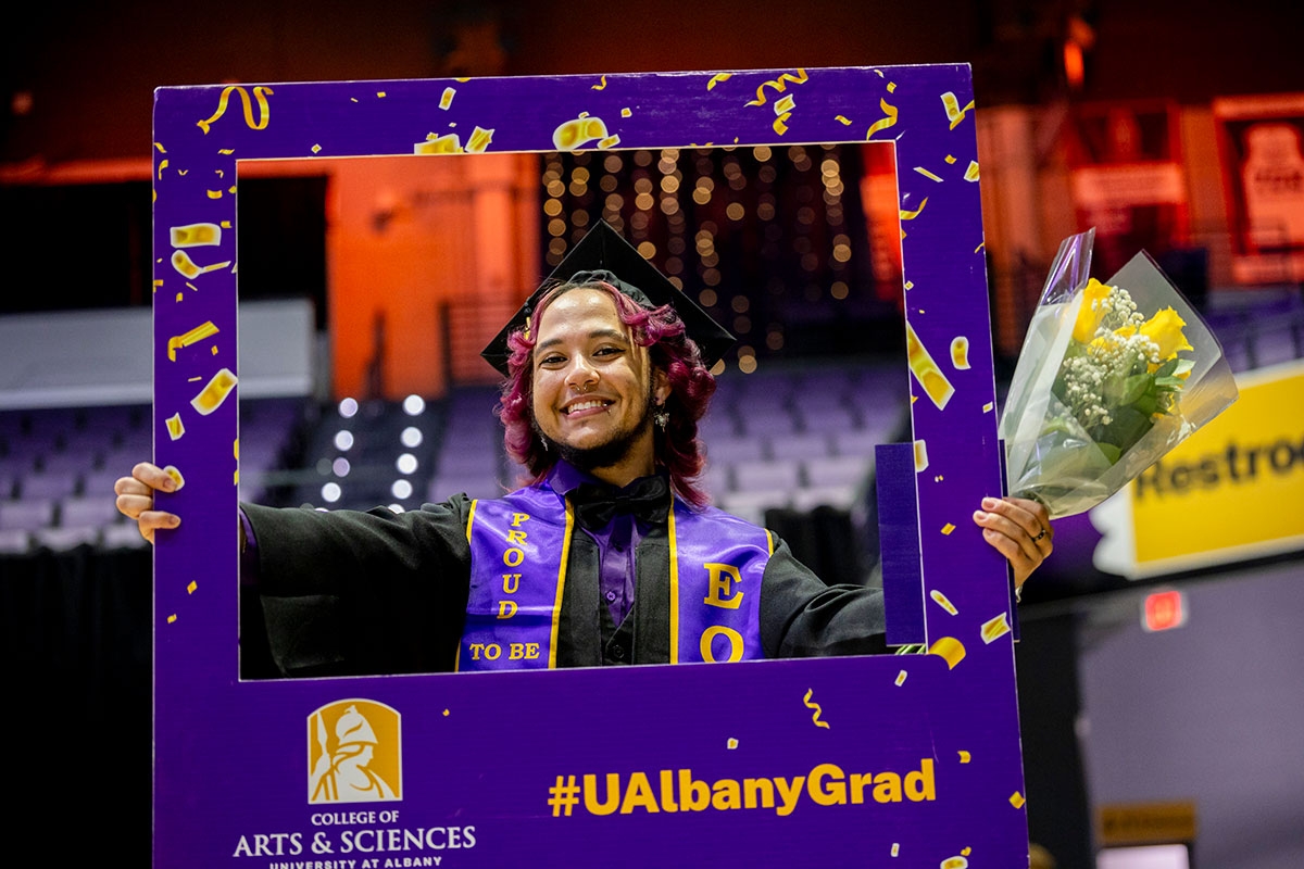 Student in full regalia posing inside of a border that says #UAlbanyGrad