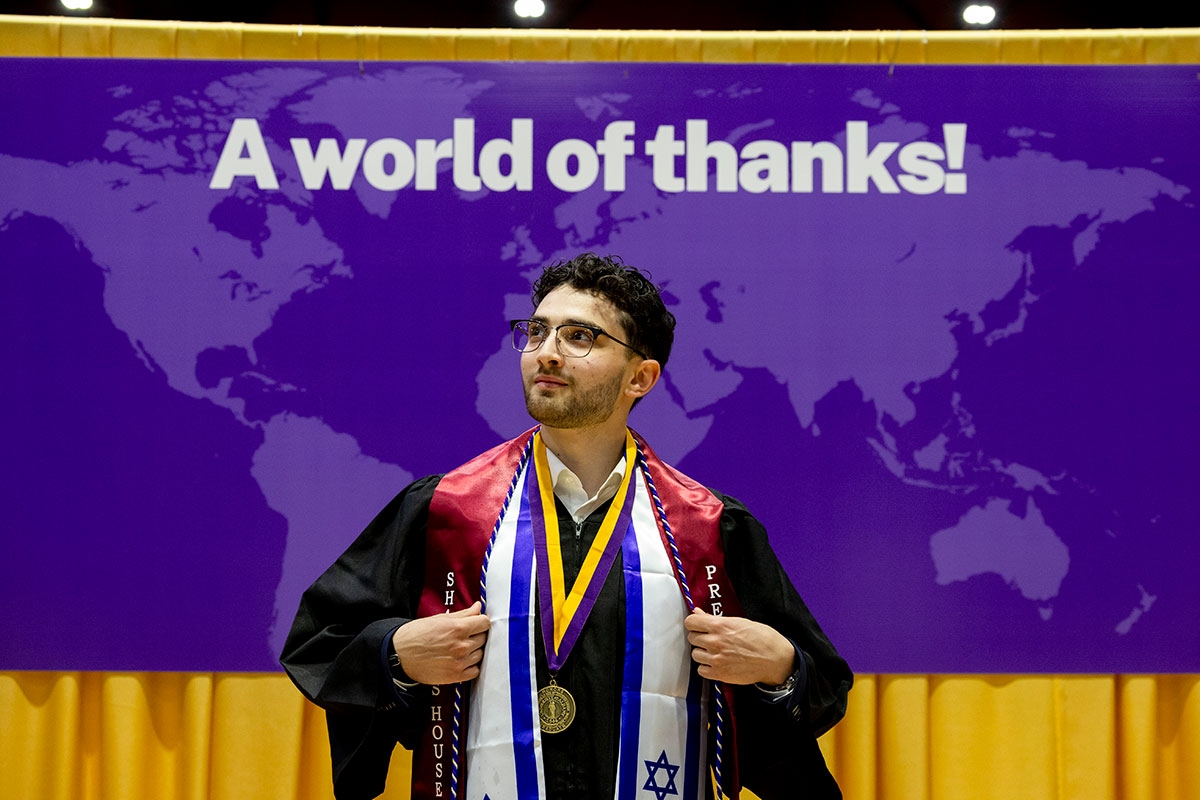 Student in regalia posing in front of a sign that says A world of thanks!