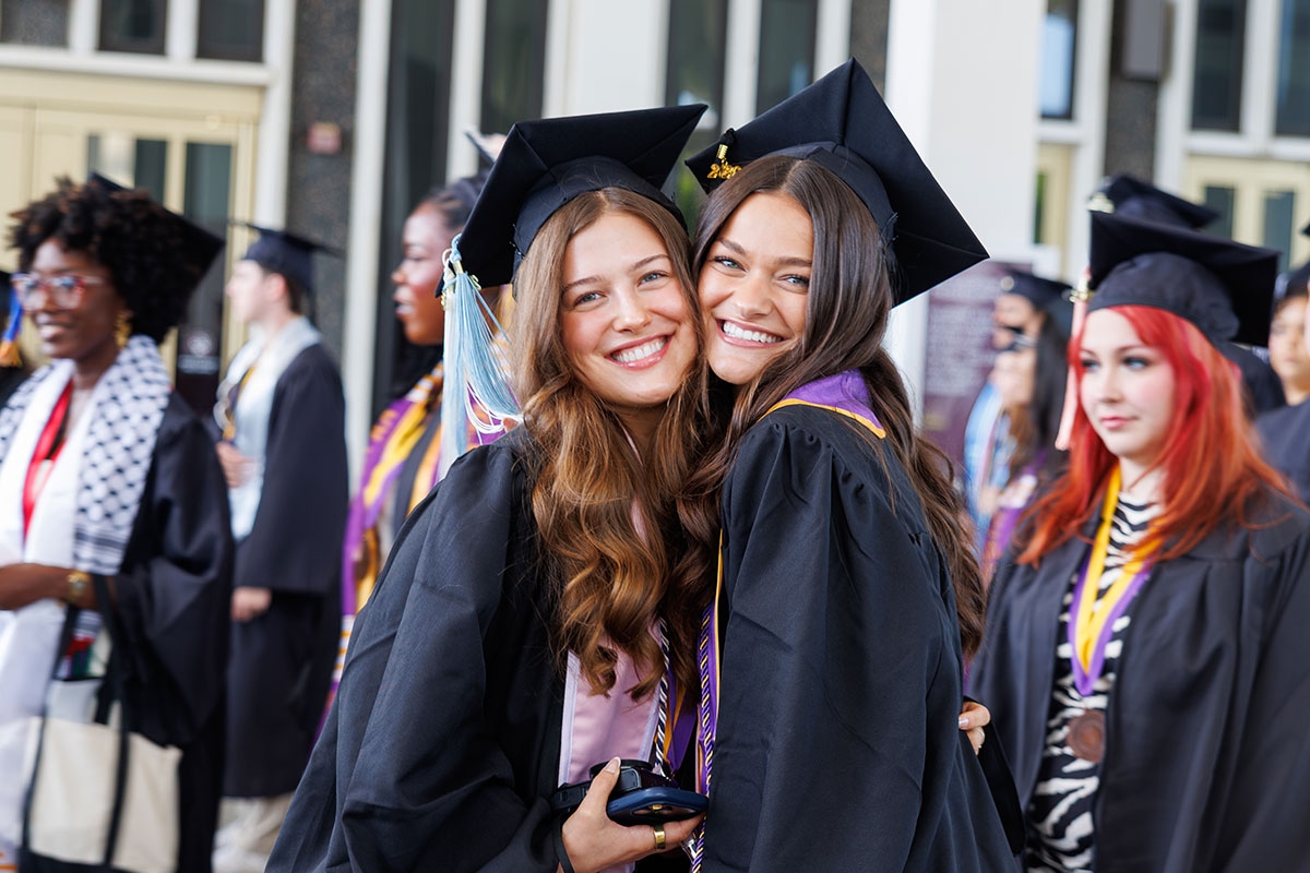 Two female students in full regalia embracing and smiling.