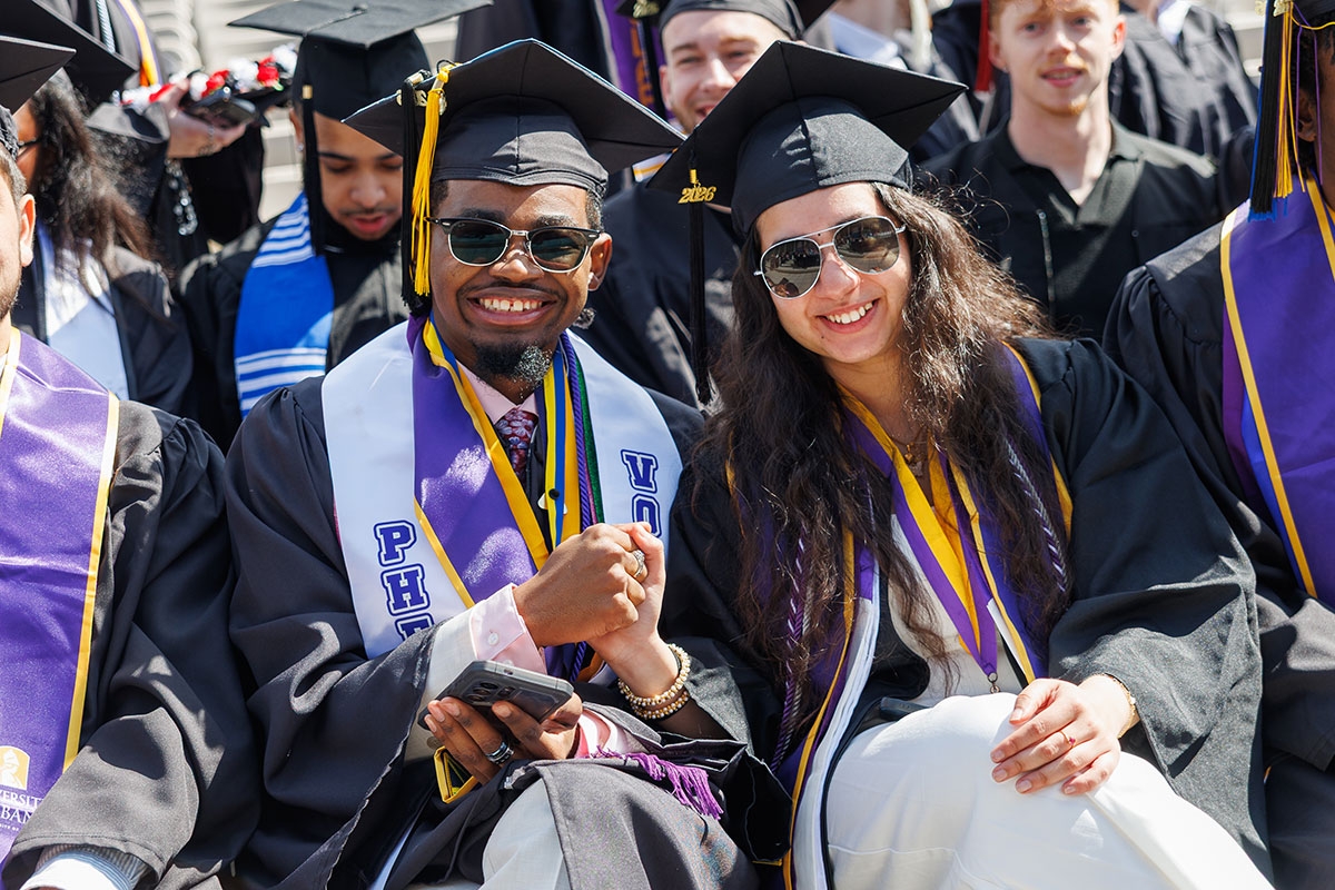 Two students in full regalia holding hands and smiling at Commencement.