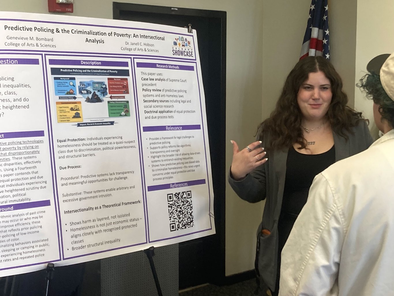 One individual stands next to a project poster talking to another individual.