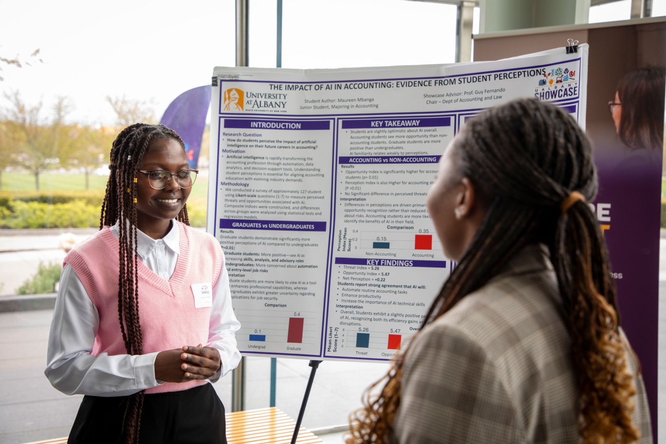 A student presenter stands in front of her poster and smiles as she speaks with a Showcase attendee about her research into AI's impact on accounting.