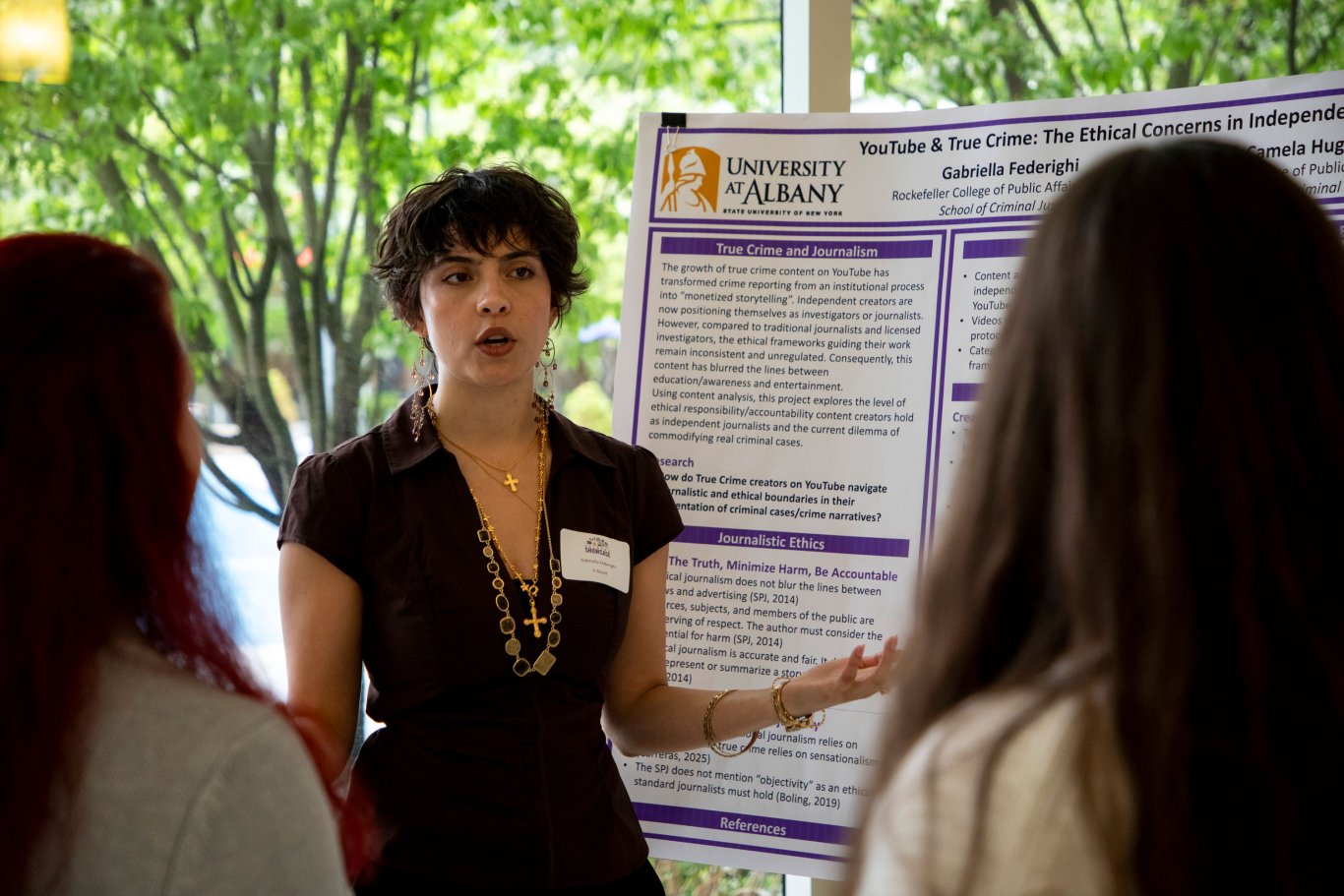 A student presenter gestures to her poster on YouTube and True Crime as she speaks to two Showcase attendees.