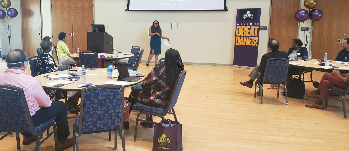 Woman stands beside a lectern, addressing the attendees of the BILPOC faculty mentoring group during the group's inaugural meeting held in the UAlbany campus center. 