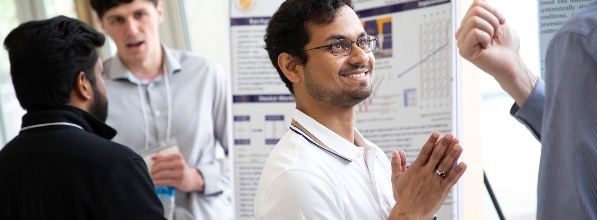 A student smiles and presses his palms together while standing in front of a poster board at Showcase 2023.