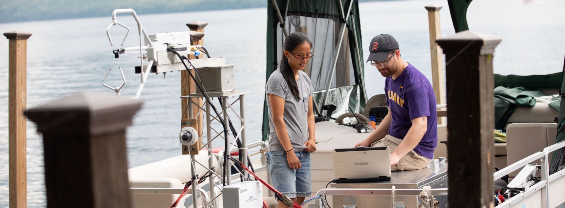 A graduate student and a researcher look at a computer monitor while taking measurements from a boat on Lake George.