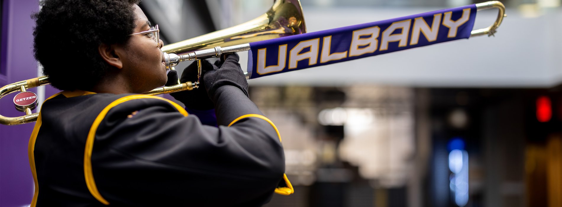 A student plays a trombone that has a slide cover that reads "UAlbany" in purple, white and gold.