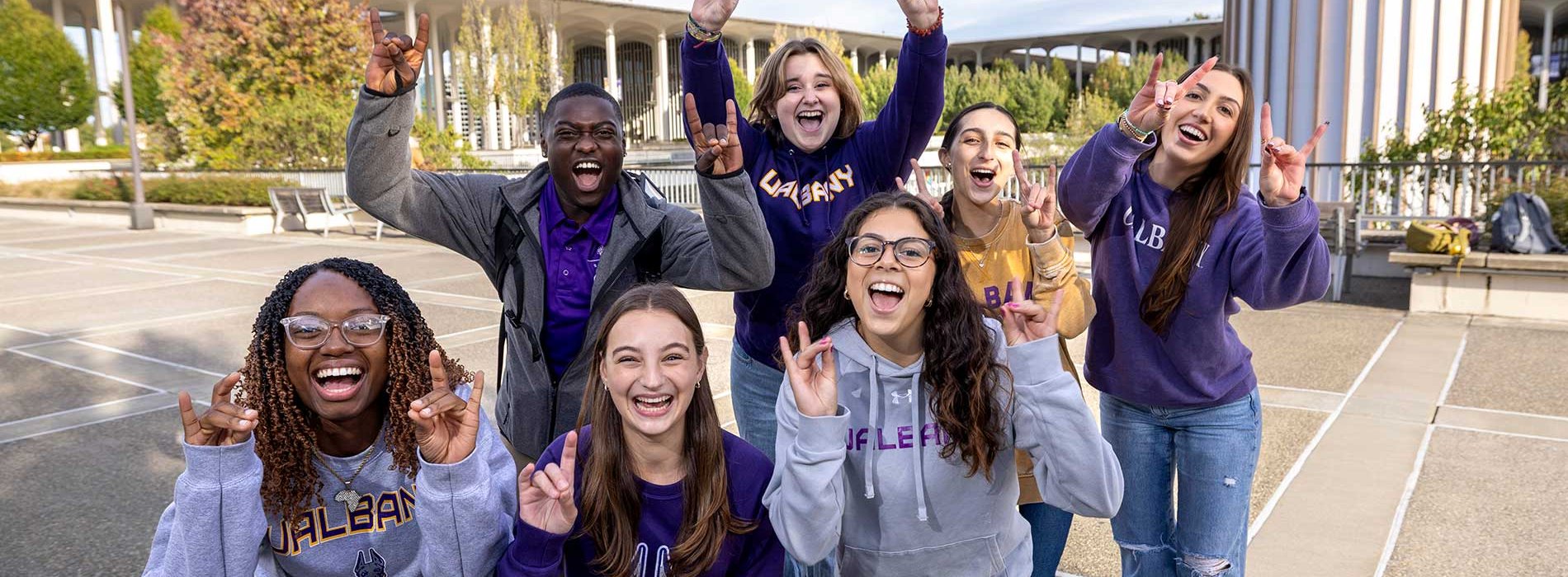 Seven students outside on the podium making Damien signs with their hands.
