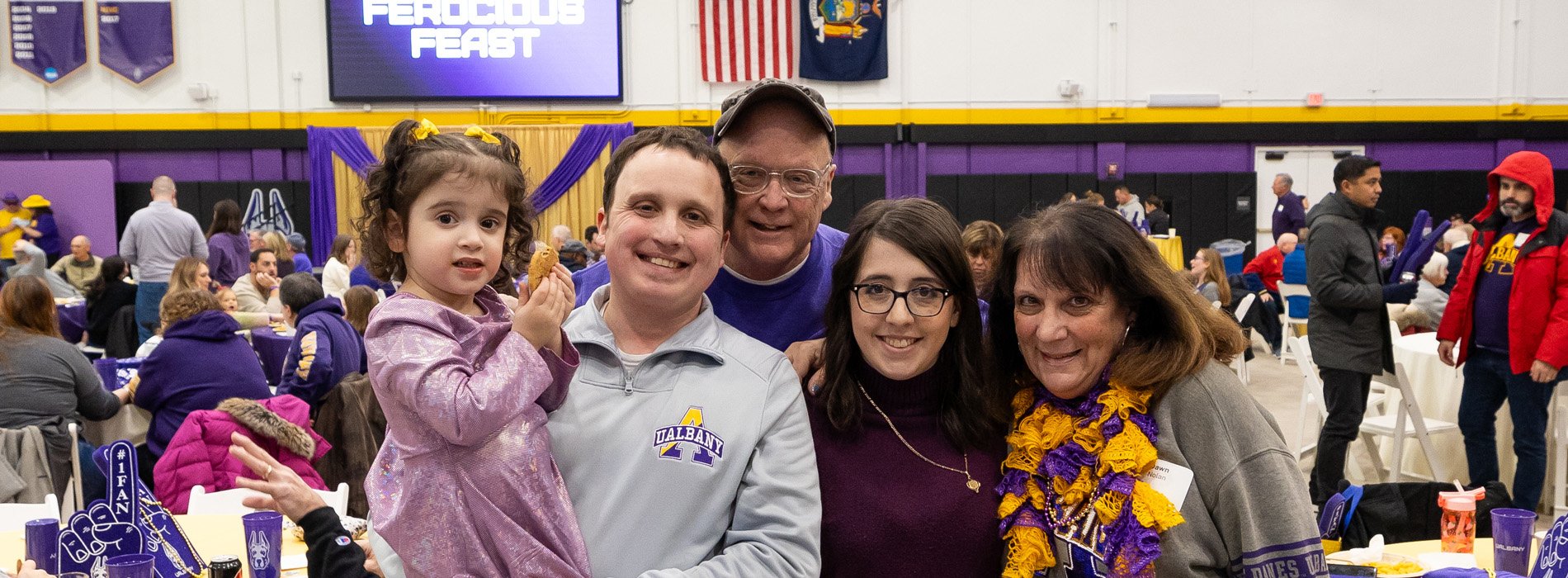 A family of five wearing UAlbany shirts at an event inside a gymnasium.