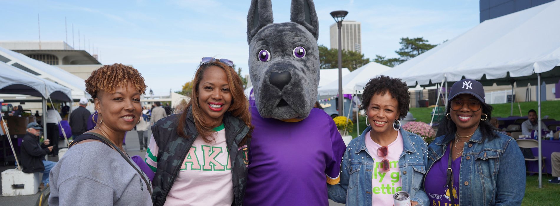 A group of Alpha Kappa Alpha sorority alumni pose with Damien the Great Dane at the football stadium.