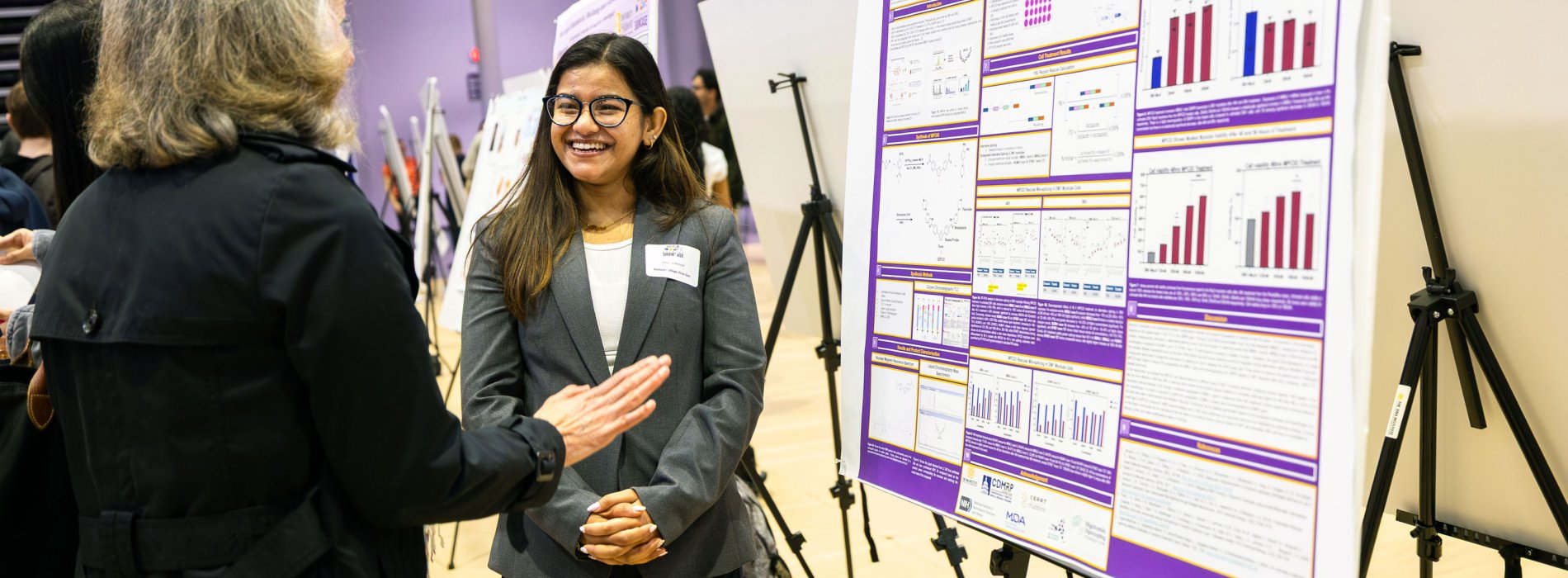 A student presenter smiles while speaking with a Showcase attendee admiring her research poster.