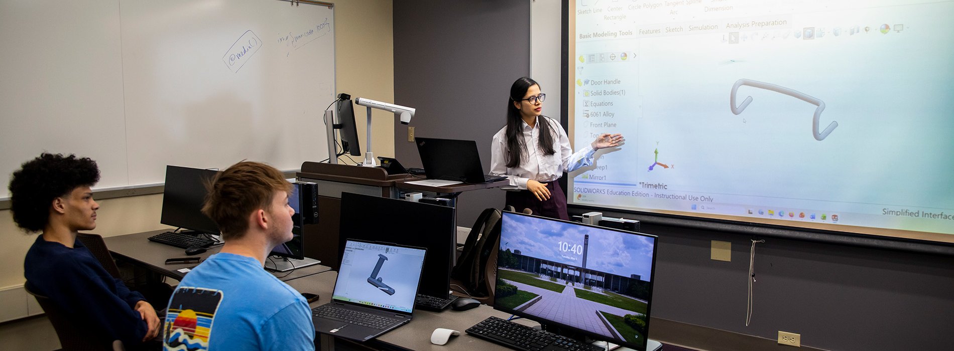 An instructor teaches a class of students in the MME program.