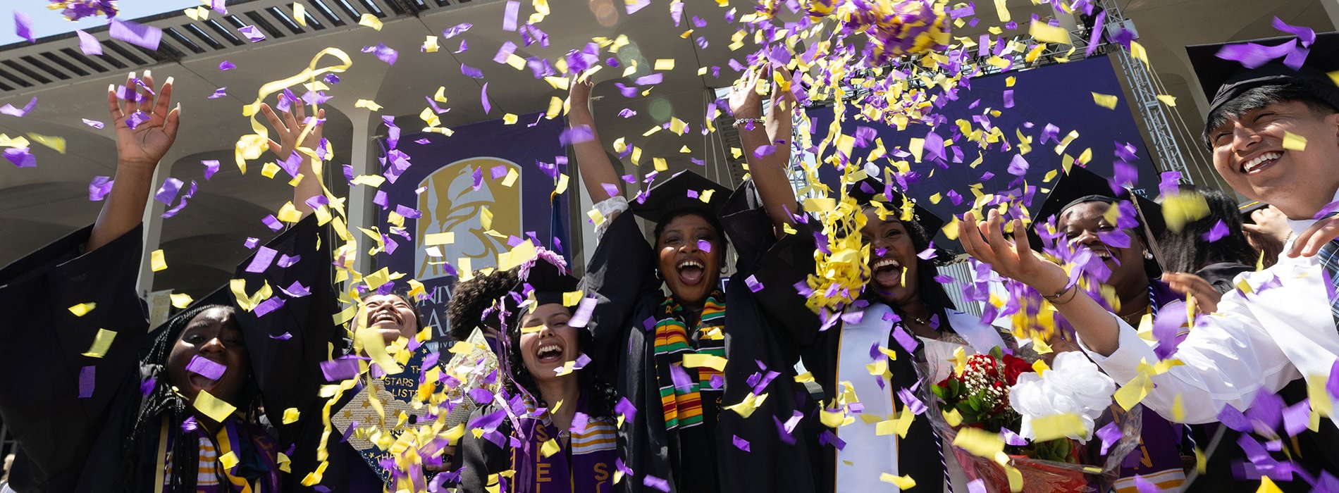 A group of students in full regalia celebrating at commencement by throwing confetti in the air.