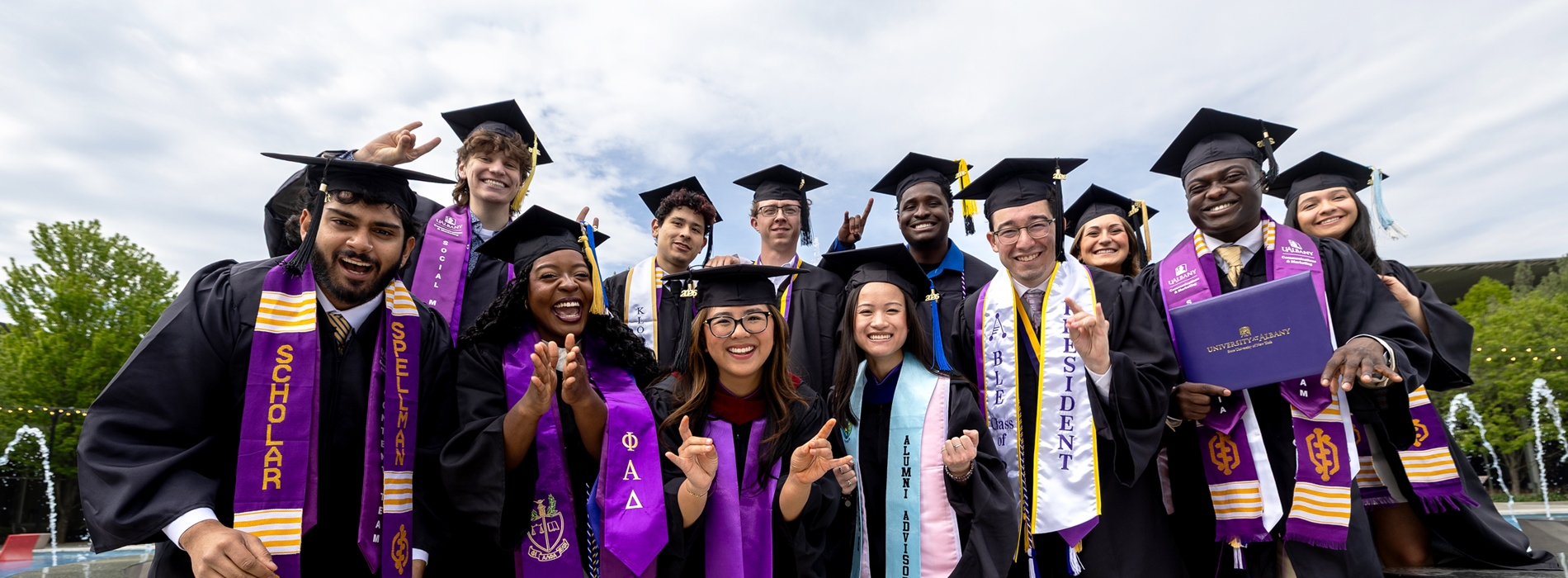 A large group of UAlbany class of 2026 graduates in caps and gowns smiling at the camera