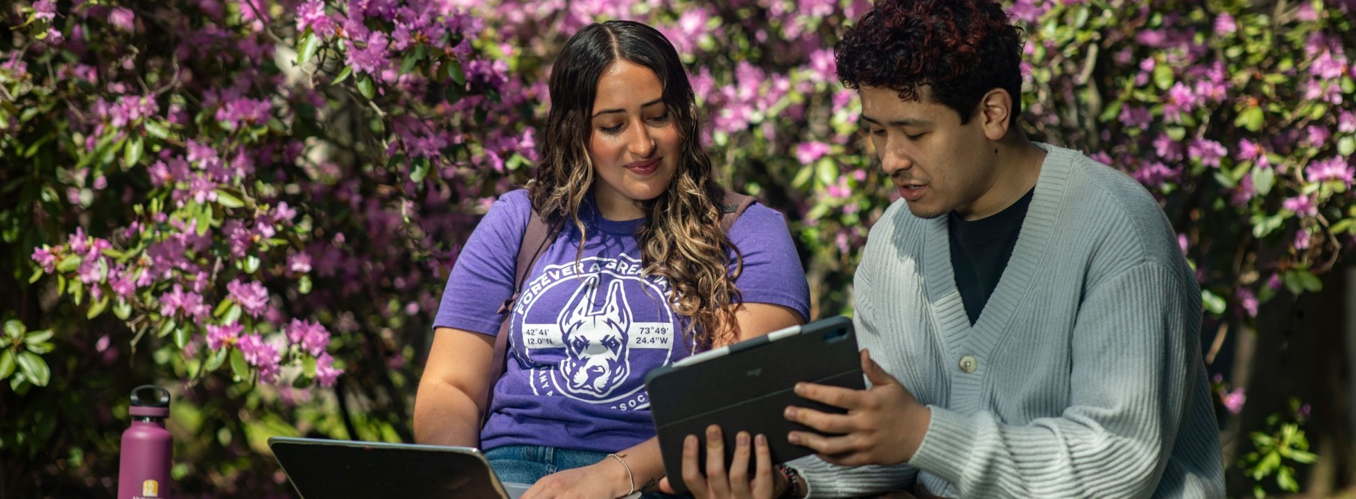 Two students sitting outside and looking at a tablet screen.