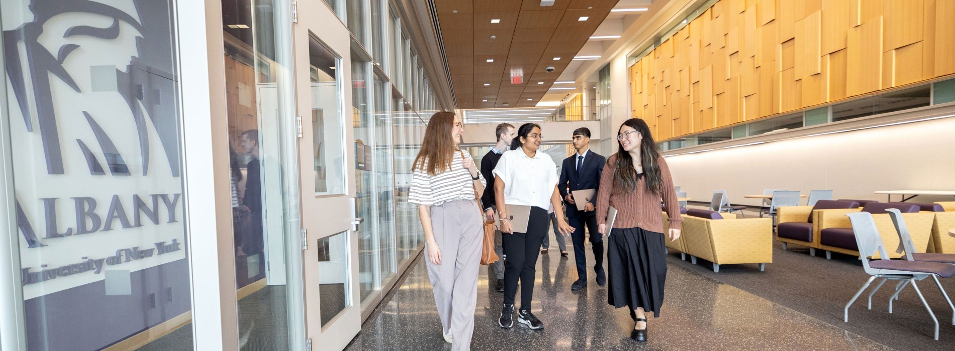 Five graduate students chat as they walk down a hallway.