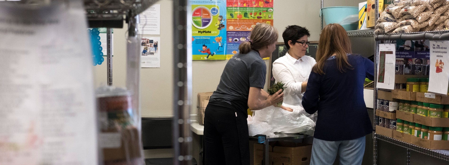 Three adults work inside a food pantry stocking shelves.