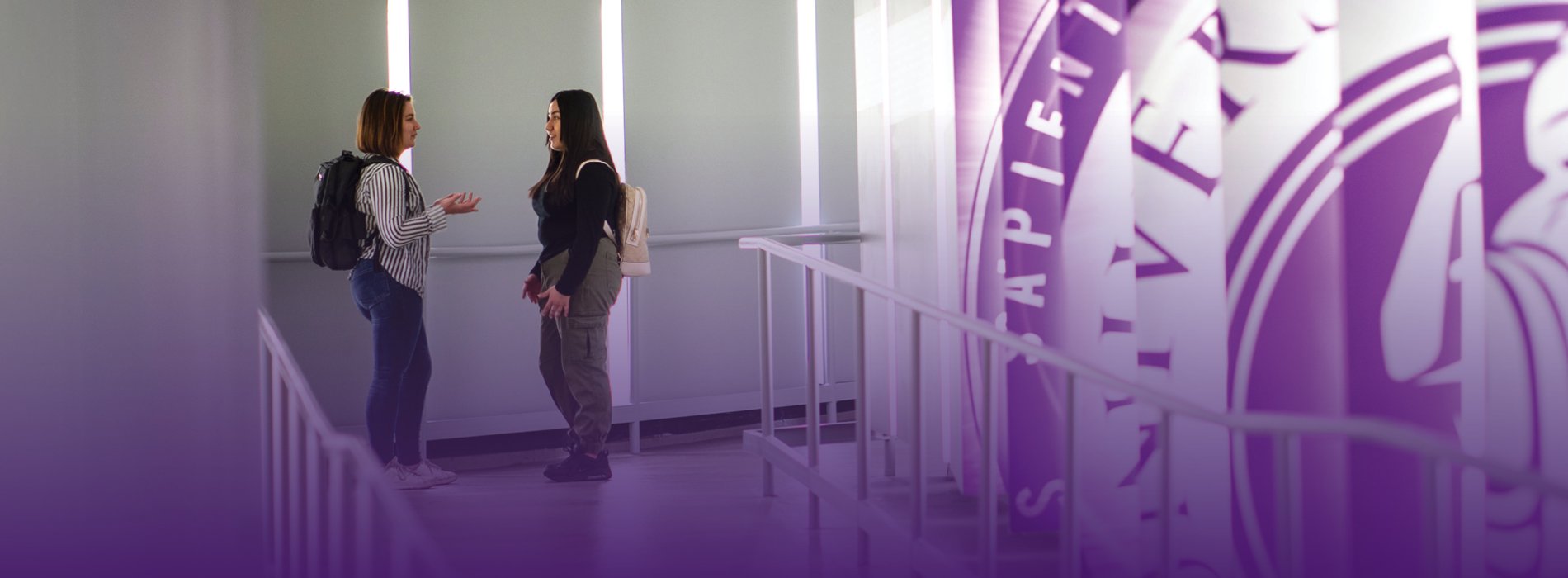 Two people talk in the donor tunnel of the Massry School of Business building.