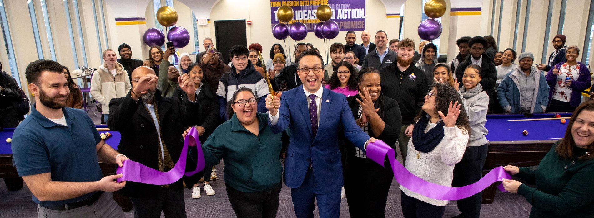 Student Affairs leadership cheers and smiles as they cut a purple ribbon inside UAlbany's new game room.