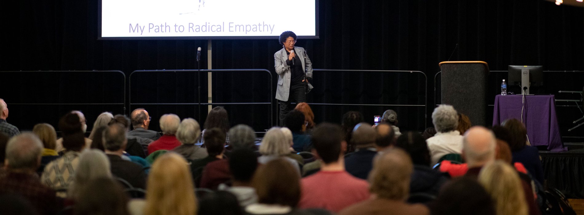 Terri Givens stands on stage before a presentation slide that says "My path to radical empathy," and speaks to her a seated audience using a microphone.
