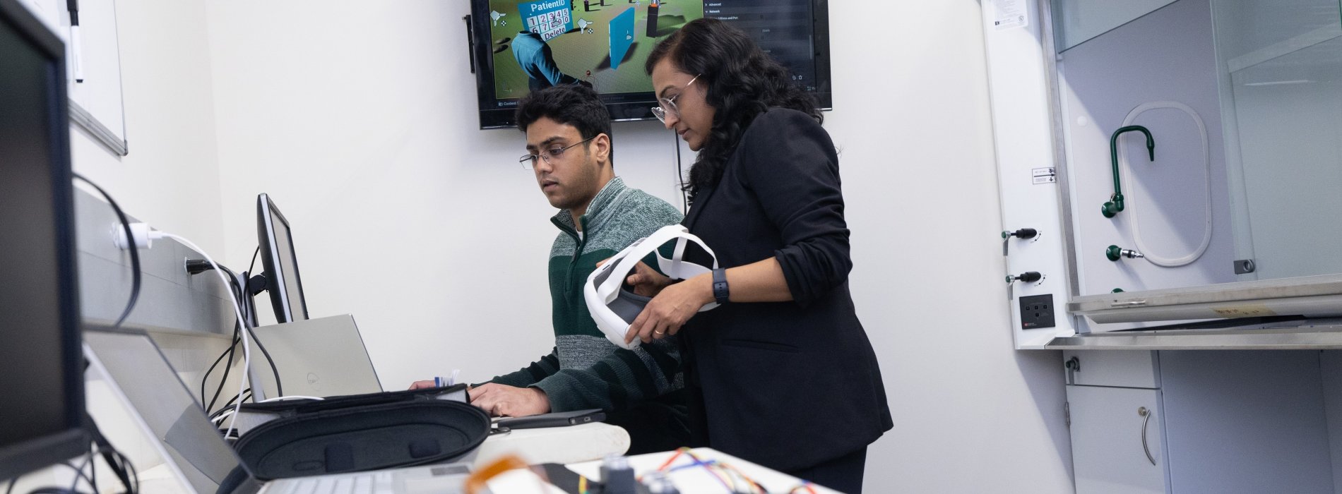 Student and a faculty member working together working in a lab with computers and a virtual reality headset.