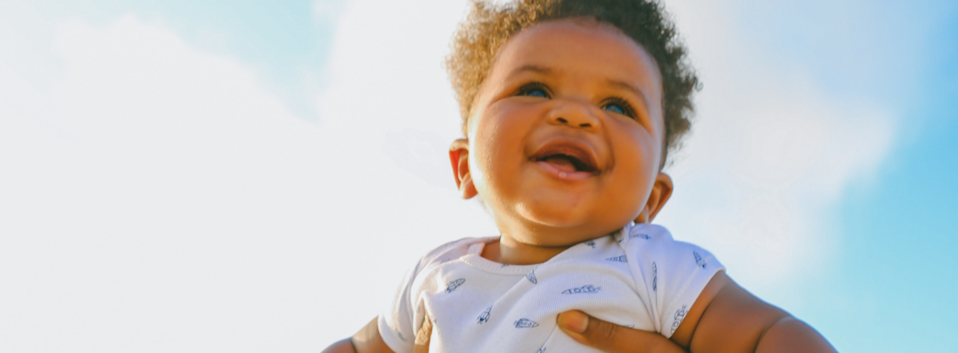 A baby is held up against the blue sky.