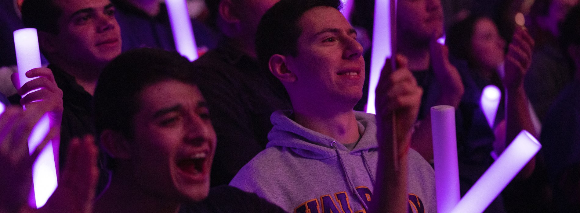 Students hold purple glow sticks as they stand and cheer for a UAlbany team