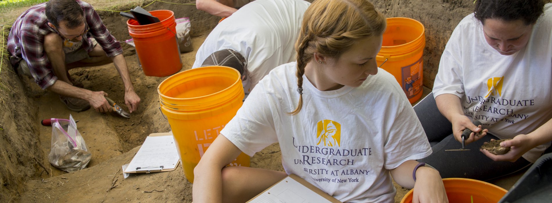Five students wearing Undergraduate Research t-shirts excavate artifacts at the archaeology dig