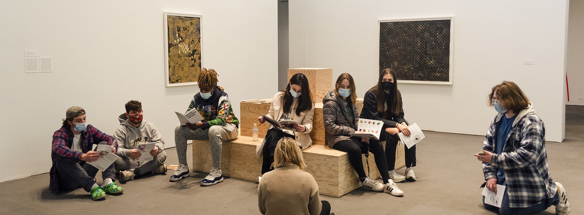 Masked students sitting on a plywood pyramid sculpture