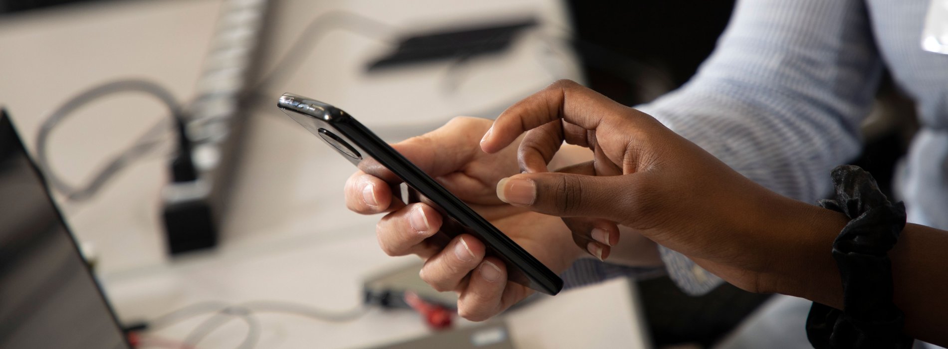 One person's hand holding a black cell phone and the other person's hand poised over the screen.