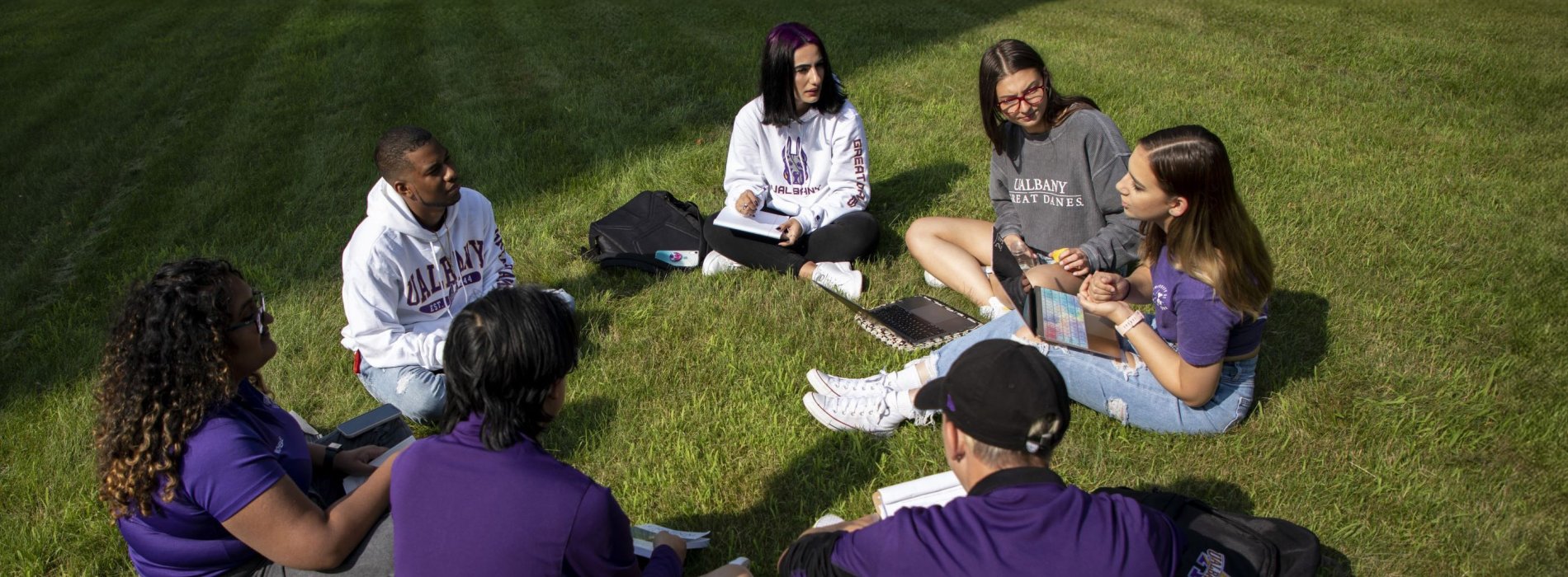 CEHC Student Ambassadors sitting in a circle in discussion on a lawn on UAlbany's campus.