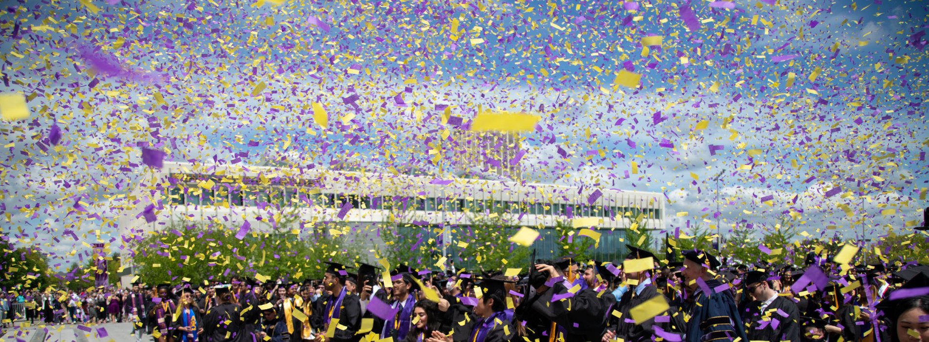 Purple and yellow confetti falls upon celebrating UAlbany graduates in Commencement regalia.