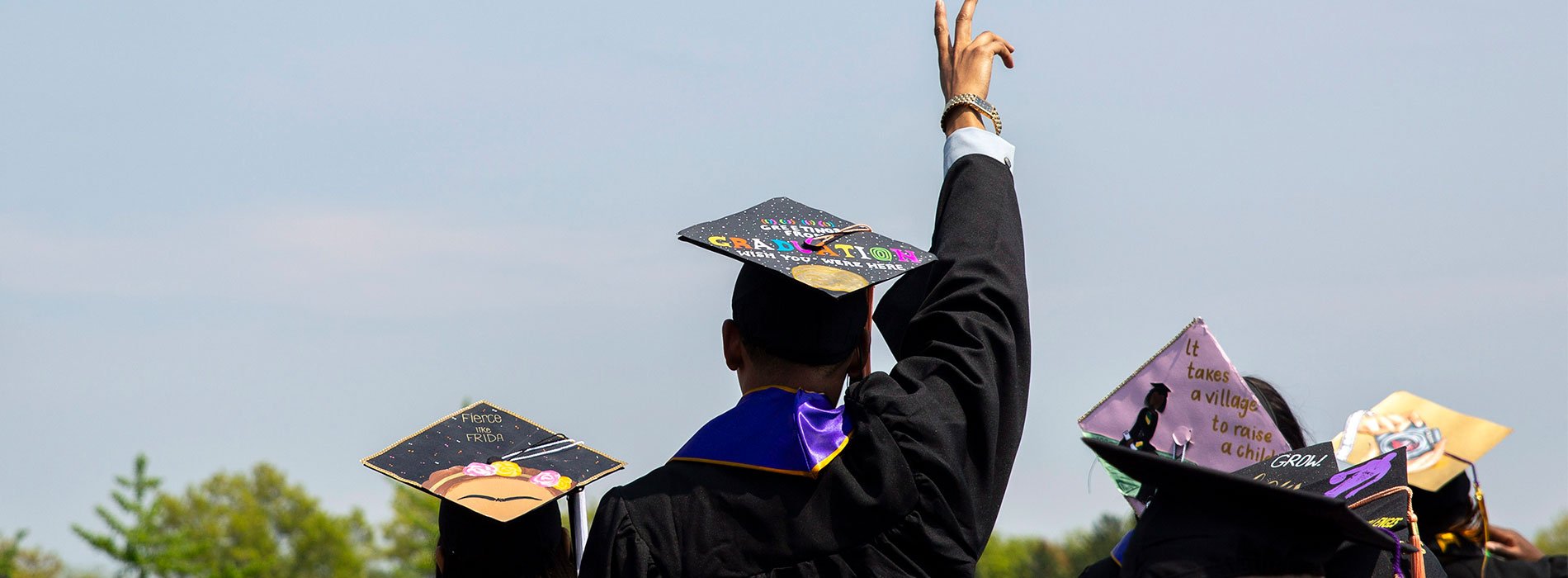 A graduate raises his hand with his back to the camera.